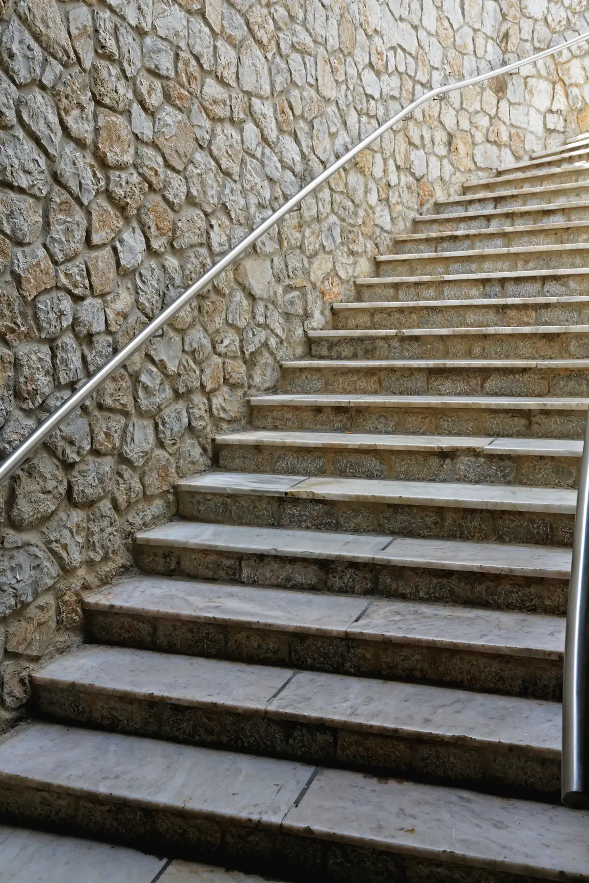 Escada externa de pedra com corrimão de inox ao lado de muro de pedra